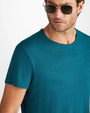 A close-up shoulder level image of a man wearing a teal blue crewneck T-shirt with square aviator glasses.