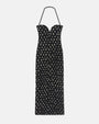 A long, black dress with a sweetheart neckline and a halter neck strap in front of a white background. The dress features an all-over pattern of small white spots.