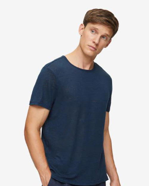 An angled knee-up view of a model with one hand in his pocket wearing a navy crewneck T-shirt with blue bottoms. The background is plain white.