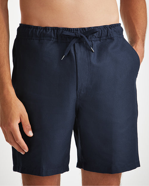 A close-up hip-level view of a shirtless model wearing a pair of navy-blue shorts with an elastic waistband and drawstrings.