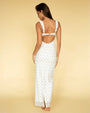 The backside view of a brunette model wearing a long, form-fitting dress with thin straps and shoulder bows, featuring an open back design and a small blue scattered pattern. The background is yellow.