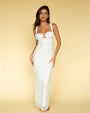 A full body view of a barefoot brunette model standing against a yellow background, wearing a long white form-fitting dress with thin straps and shoulder bows, featuring an empty space design at the chest, and a colorful pattern with a small blue scattered pattern.