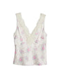 A white floral-patterned tank top adorned with pink flowers, a V-neck, and delicate lace trim with scalloped edges along the neckline and straps. The shirt is placed against a white background.