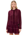 Person wearing a sheer, long-sleeved burgundy blouse with vertical lace stripes and front buttons, paired with a layered burgundy skirt featuring lace detailing.
