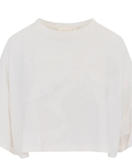 A close-up frontal shot of a cropped white; loose-fitting top placed against a white background. The sleeves are about the same length as the body.