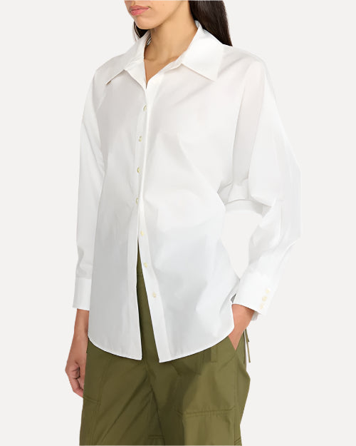 A close-up torso shot of a dark-haired model wearing a white long-sleeve button down top with a pointed collar. The person is wearing army green pants as well while standing against a white background.