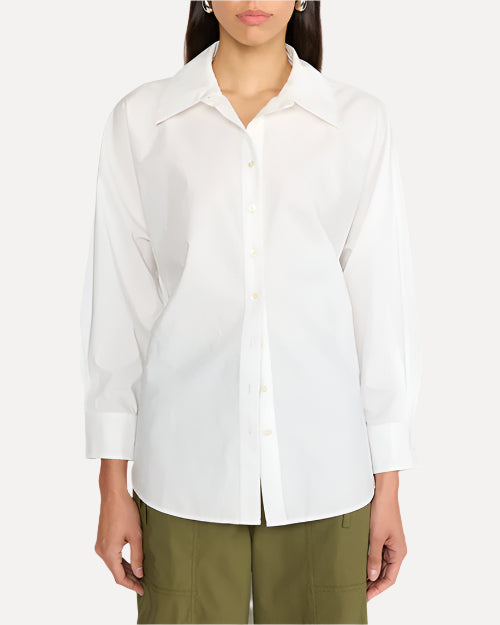 A dark-haired model in front of a white background, wearing a white long-sleeve button down top with a pointed collar, and the person is wearing army green pants.