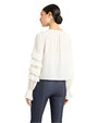 Back view of a woman wearing a white blouse with ruffled sleeves and dark jeans on a white background