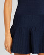 A close-up hip-level view of a navy knit dress with light sparkles and ribbed accents. The model is also wearing a silver ring, and standing in front of a white background.