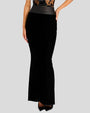 A lower-body shot of a model wearing a long, black, form-fitting skirt with a thick wrapped waistband and black pointed toe heels. The skirt is tucked into a sheer lace top with black detailing. The model is standing in front of a white background.