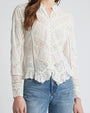 A close-up torso level view of a brunette model wearing a white, long-sleeved button-down blouse with a high collar, featuring intricate lace detailing and scalloped edges at the hem and cuffs. The background is white.