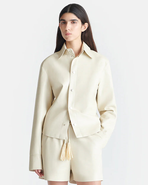A close-up shot of a brunette model wearing an Off-White long-sleeved button-down jacket with matching shorts and tasseled drawstrings.