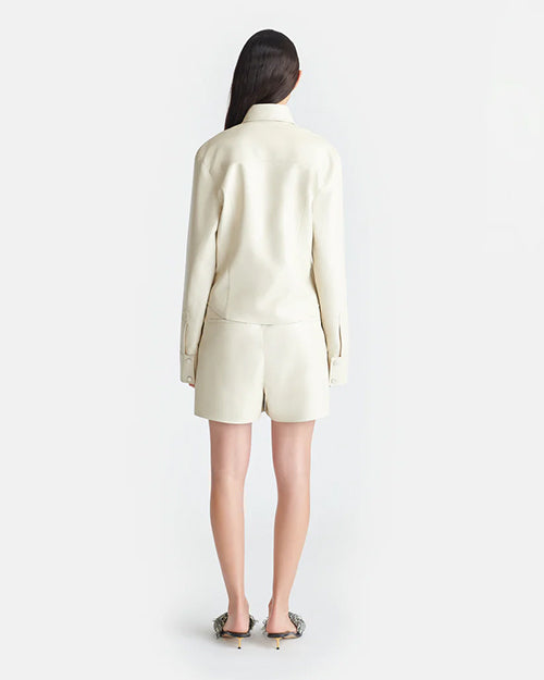 The backside view of a brunette model with her hair swept to the side, wearing an Off-White long-sleeved button-down jacket with matching shorts with tasseled drawstrings. The person is also wearing slip-on heels.