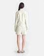 The backside view of a brunette model with her hair swept to the side, wearing an Off-White long-sleeved button-down jacket with matching shorts with tasseled drawstrings. The person is also wearing slip-on heels.