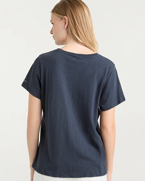 The backside view of a blonde model with her hair swept to the side wearing a navy crewneck t-shirt. The background is plain and white.