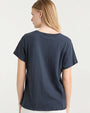 The backside view of a blonde model with her hair swept to the side wearing a navy crewneck t-shirt. The background is plain and white.