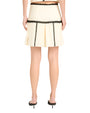 Back view of  a waist down image of a person wearing a cream pleated skirt with black zigzag stitching and black  heels