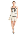 Person wearing a white two-piece set with black trim, featuring a sleeveless top and pleated skirt with black heels.