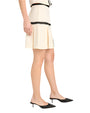 Side view of the bottom of a person wearing a cream-colored dress with black trim on a light background