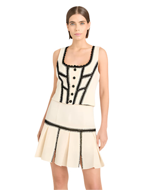Person wearing a white two-piece set with black trim, featuring a sleeveless top and pleated skirt.