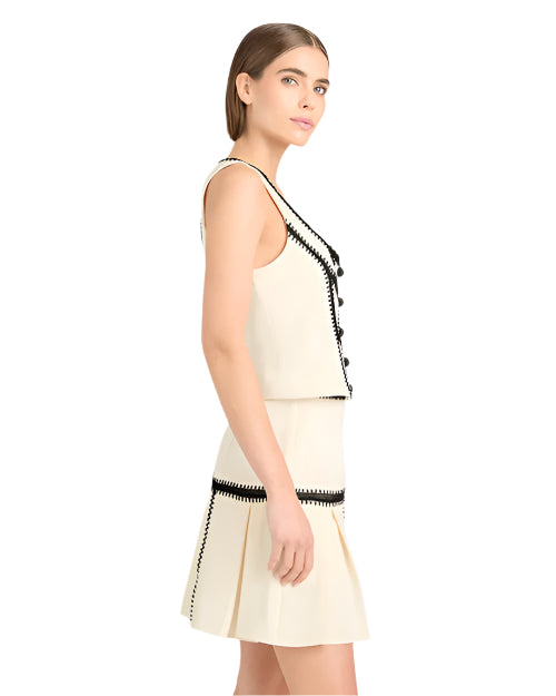 Side view Back view of a person in a sleeveless cream two piece set (skirt and top) with black zigzag trim, against a white background.