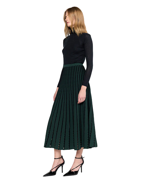 Woman wearing a black long-sleeve top and green pleated skirt on a white background