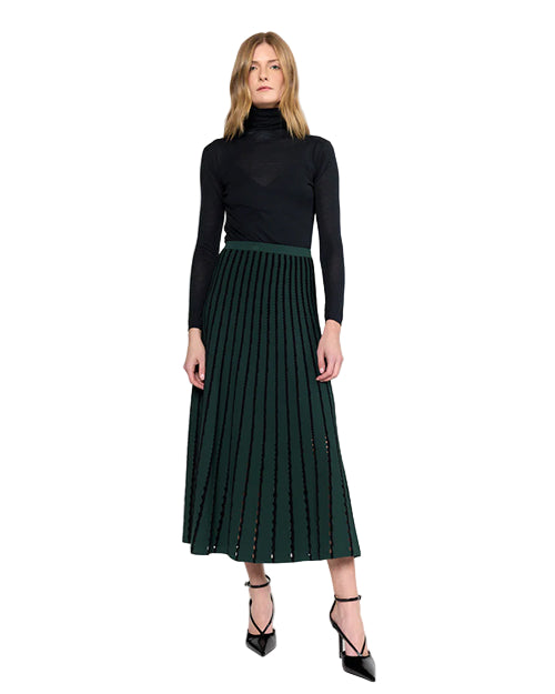 Woman wearing a black turtleneck and green and  black pleated skirt with black heels on a white background