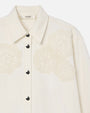 A close image of a collared white jacket with doily/floral embroidery on the left and right side of the upper chest. The jacket has silver buttons and a tag in the inner collar reading "FRAME".