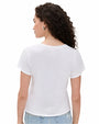 The backside view of a curly-haired model with her hair pushed to the side, wearing a white t-shirt. The shirt is worn with blue jeans and silver hoop earrings in front of a white background.