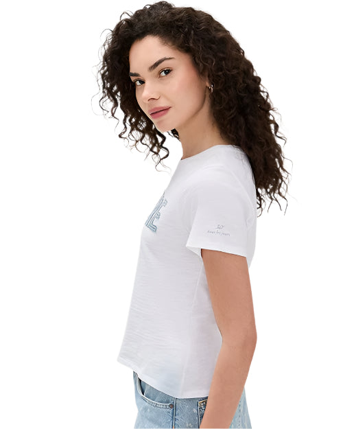A side view of a curly-haired brunette model wearing a white t-shirt with blue letters on the front paired with blue jeans.