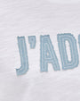 A close-up image of the word "J'AD" written in large, bold blue letters with a slightly worn look on a piece of white fabric.