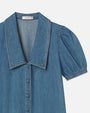 A close-up shot of a blue denim dress with short, puffed sleeves, a large, pointed collar, and denim buttons down the front, placed in front of a white background.
