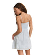 The backside view of a curly-haired model looking behind her, wearing a white, sleeveless dress with thin straps, a fitted bodice, and the skirt of the dress is slightly flared with subtle pleats and lace accents.