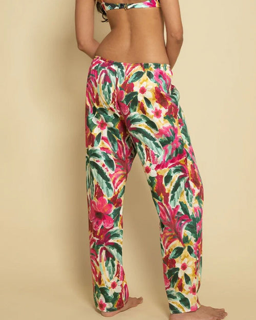 A backside, legs-only shot of a model wearing a matching watercolor floral pattern set consisting of colorful bikini top and loose-fitting pants with an elastic waistband and drawstrings. The model is barefoot and standing in front of a yellow background.
