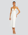 A full body view of a brunette model with her hand on her hip wearing a white midi dress with thin straps lined with pearls and cut-out square details along the upper waistline. The model is also wearing white open-toed heels, and gold hoops, standing in front of a white background.