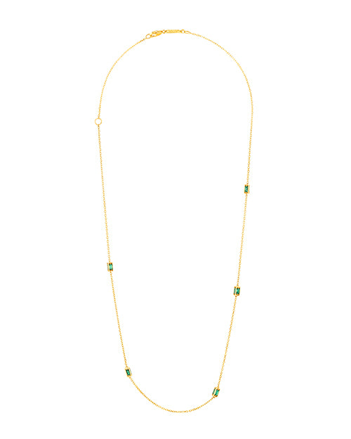 A gold necklace with a thin chain and small green rectangular gemstones around it. The necklace is placed in front of a white background.