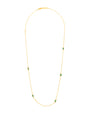 A gold necklace with a thin chain and small green rectangular gemstones around it. The necklace is placed in front of a white background.
