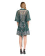 Back view of a person wearing a green dress with intricate floral and paisley patterns. The dress has short sleeves and a tie at the waist. The person is also wearing black high-heeled shoes.