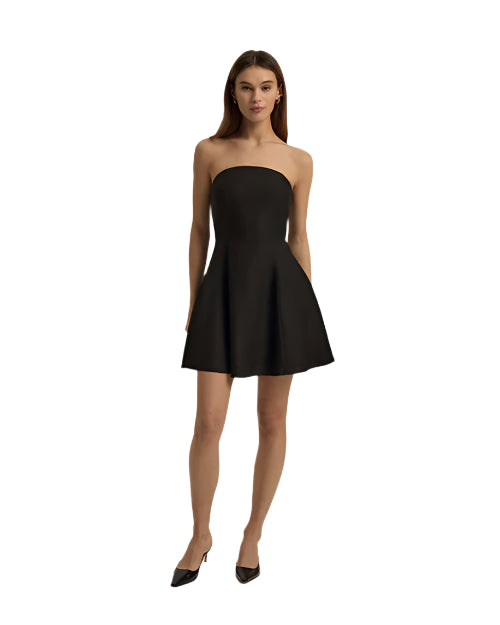 A full body view of a model wearing a strapless black dress that flares out at the bottom. The model is also wearing black pointed-toe shoes and standing against a plain white background.