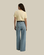 The backside view of a person wearing a light yellow short-sleeved t-shirt tucked into high-waisted blue jeans with a black belt. The background is plain and beige.