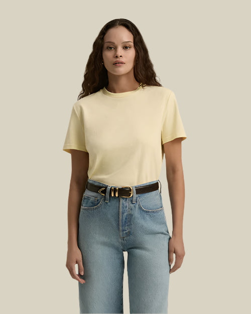 A person wearing a light yellow short-sleeved t-shirt tucked into high-waisted blue jeans with a black belt. The background is plain and beige.