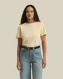 A person wearing a light yellow short-sleeved t-shirt tucked into high-waisted blue jeans with a black belt. The background is plain and beige.