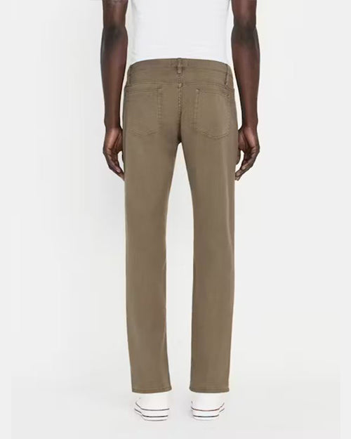 A lower body backside shot of a model wearing a white shirt tucked into a pair of green jeans with silver buttons, and white shoes. The model is standing in front of a white background.