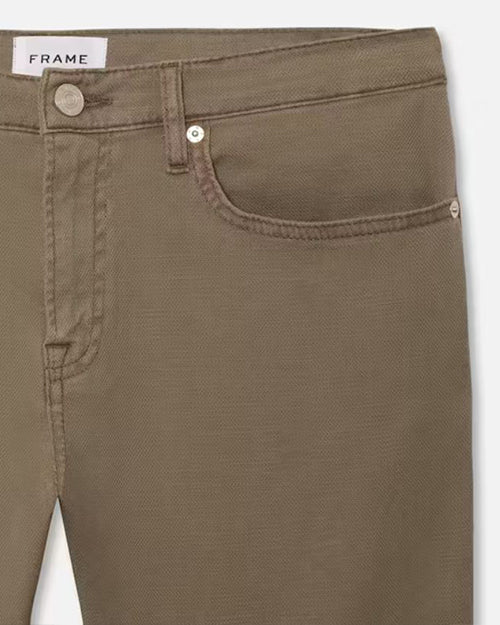 A close-up hip level view of a pair of green jeans with silver buttons, and a white rectangular tag reading "FRAME" on the inner waistline.