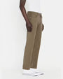 An angled lower body shot of a model wearing a white shirt tucked into a pair of green jeans with silver buttons, and white shoes. The model is standing in front of a white background.