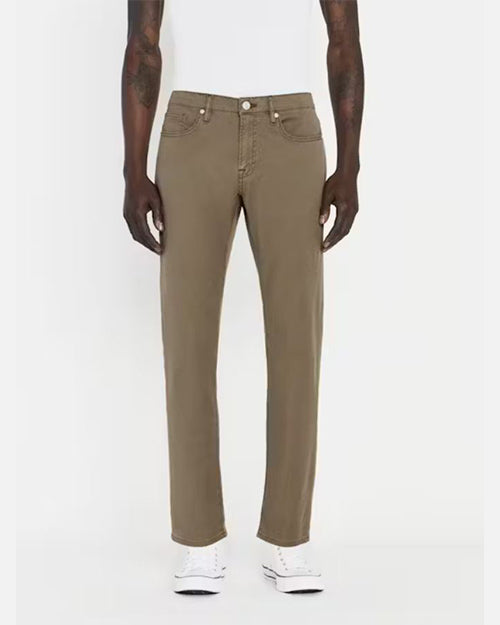A lower body shot of a model wearing a white shirt tucked into a pair of green jeans with silver buttons, and white shoes. The model is standing in front of a white background.
