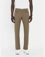 A lower body shot of a model wearing a white shirt tucked into a pair of green jeans with silver buttons, and white shoes. The model is standing in front of a white background.