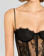 A close-up chest level view of a short-haired model wearing a black lace corset with thin straps and a lace bodice, standing against a white background.