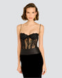 A short-haired brunette model in front of a white background, wearing a long dress with a black lace corset top, thin straps and intricate lace detailing around the waist, and the lower half is a velvet black skirt.