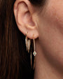 A close-up image of a brunette models' earring wearing a gold hoop earring with jewel adorned spikes hanging from the hoops, and thinner gold hoop under it decorated with a diamond jewel design in the center.